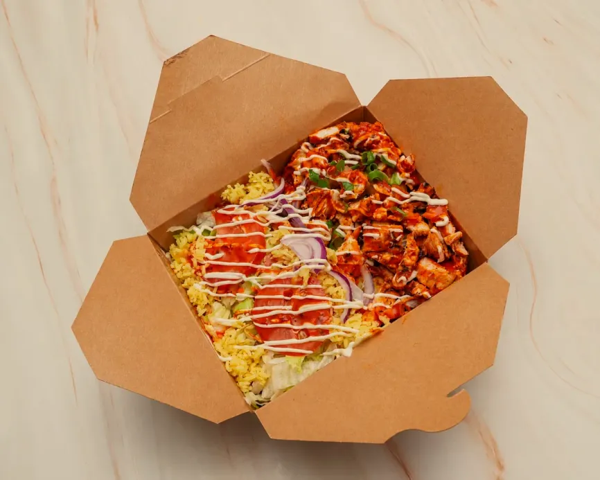 A chicken rice box: flame-grilled chicken over spiced rice with salad and sauce