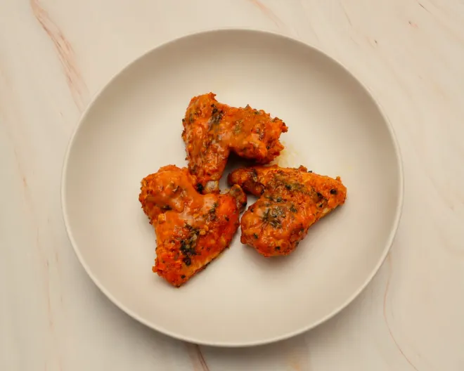 Three peri peri wings on a plate, sauced and flecked with herbs